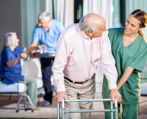 Happy Caretaker Assisting Senior Man In Using Zimmer Frame